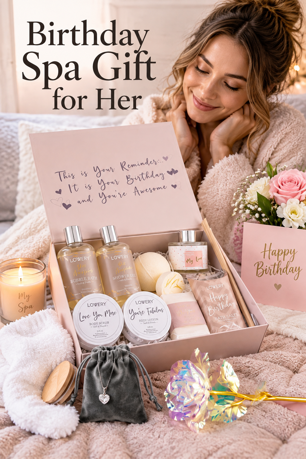 A blush pink birthday spa gift box arranged on soft neutral bedding while a woman in a plush robe smiles behind it. The open box shows LOVERY bubble bath, shower gel, body scrub, body lotion, bath salts, candle and bath items. A heart necklace in a dark pouch, iridescent decorative flower, white fuzzy socks, fresh pink and white flowers, and a Happy Birthday card surround the box. Headline reads “Birthday Spa Gift for Her.”
