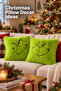 Vertical Christmas living room scene with two bright lime-green shaggy square pillow covers featuring black mischievous face designs on a cream sofa. A lit Christmas tree with red and gold ornaments fills the background beside mantel greenery, stockings, candles, and warm holiday lights. Red knit and plaid cushions, a chunky cream throw, greenery, books, and a wrapped gift complete the cozy setting. White headline text at the upper left reads “Christmas Pillow Decor Ideas.”