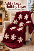 Dark red chunky knit snowflake throw draped over a cream armchair in a cozy holiday room, with the headline Add a Cozy Holiday Layer.