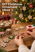 Vertical holiday craft scene with the headline “DIY Christmas Ornament Ideas” in large white text at the upper left. Hands in a cream knit sweater paint a small wooden snowflake red at a warm wooden table. Natural unfinished snowflake cutouts, twine loops, a paint palette, greenery, and a bowl of ornaments surround the workspace. In the background, several wooden snowflakes hang on a lit Christmas tree beside softly blurred wrapped gifts and warm golden lights.