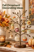 Vertical lifestyle photo of ten miniature fall-themed porcelain ornaments hanging from a bronze tabletop ornament tree on a warm autumn console. Visible pieces include a cornucopia, harvest dish, sunflower, corn, red jam jar, smiling scarecrow, green basket, tan pilgrim-style hat, white round ornament, and orange pumpkin. A candle, books, acorns, fallen leaves, plaid runner, floral arrangement, and pumpkins frame the scene. Headline reads “Fall Ornament Decorating Ideas.”