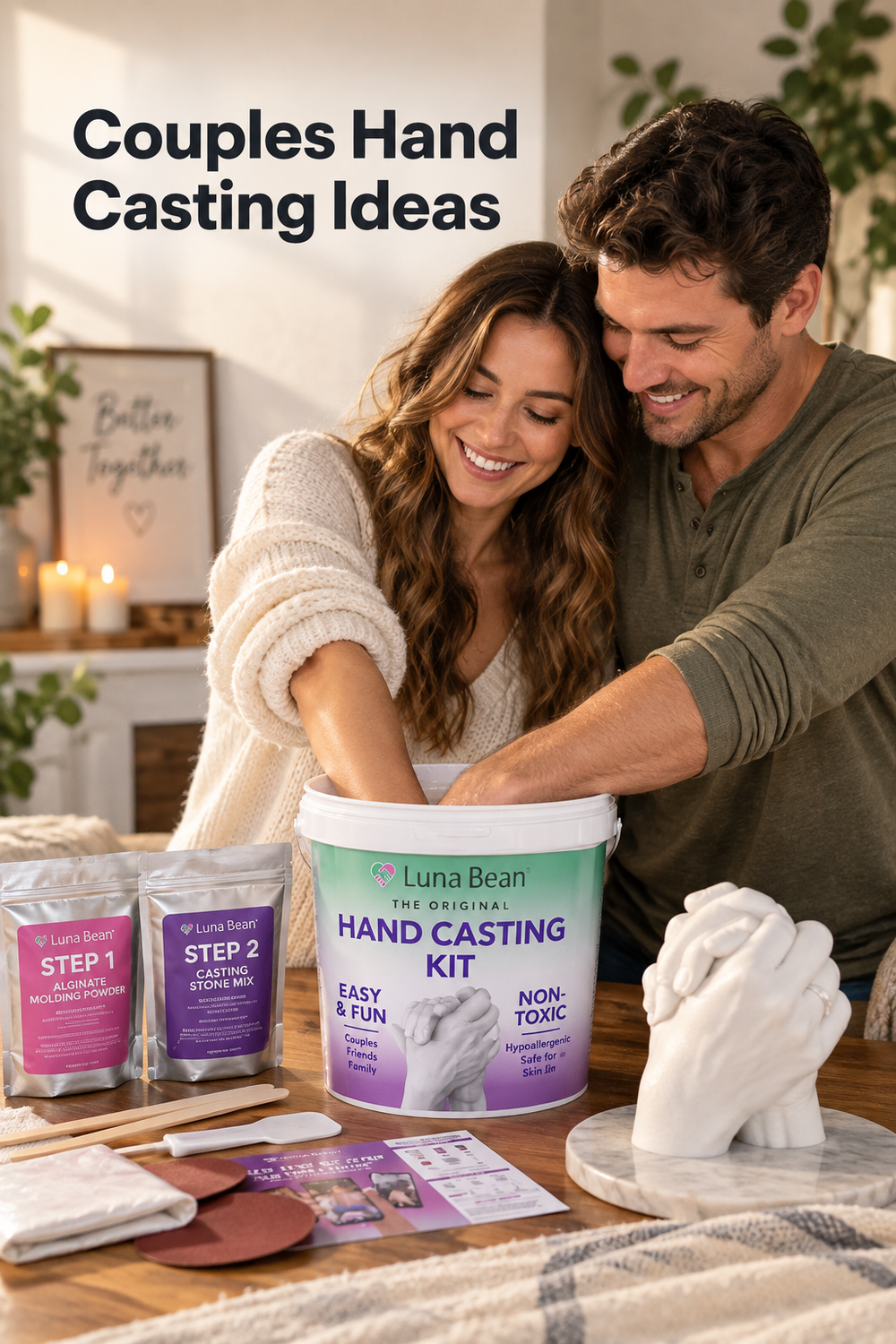 Vertical lifestyle photo of a smiling couple at a wooden table using a Luna Bean hand casting kit, with both forearms lowered into the branded casting bucket. Step 1 alginate molding powder and Step 2 casting stone mix pouches sit beside the bucket with small tools, sanding discs, an instruction card, and a finished white sculpture of clasped hands. Warm candles and greenery soften the home setting. Headline at top left reads “Couples Hand Casting Ideas.”