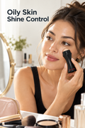 Vertical beauty photo with the headline “Oily Skin Shine Control” in dark type at the upper left. A woman with dark hair in a loose bun looks toward a round vanity mirror while rolling a black Revlon oil-absorbing face roller with a beige stone ball across her right cheek. Warm daylight highlights visible facial shine. A pink makeup pouch, brushes, compact powder, perfume bottle, and greenery sit around the bright vanity, creating an everyday makeup touch-up setting.